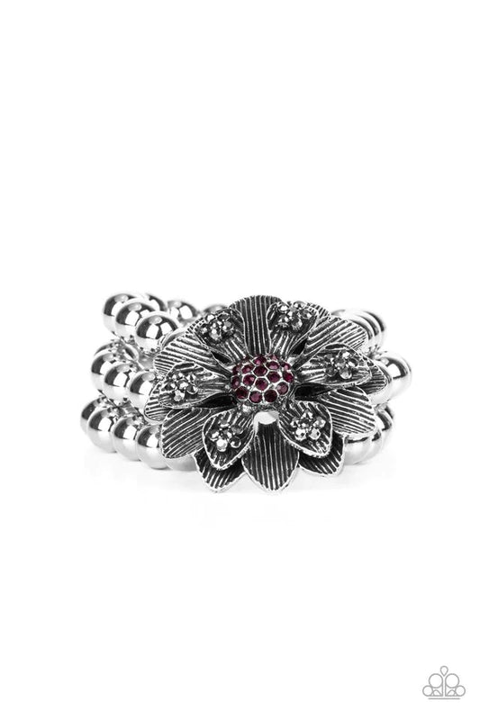 Paparazzi Accessories Botanical Bravado - Purple A daring oversized silver flower is composed of petals lined in antiqued silver and dotted with smoky hematite rhinestones. A sphere of dainty purple rhinestones creates the center of the flower as it sits