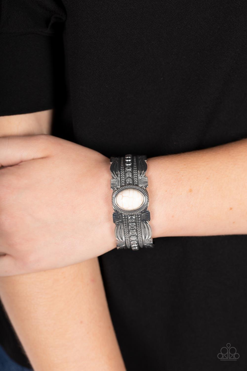 Paparazzi Accessories Desert Stroll - White An oversized oval white stone is pressed into the studded center of an ornate silver cuff stamped and embossed in tribal inspired patterns, resulting in a refreshing pop of color atop the wrist. Sold as one indi