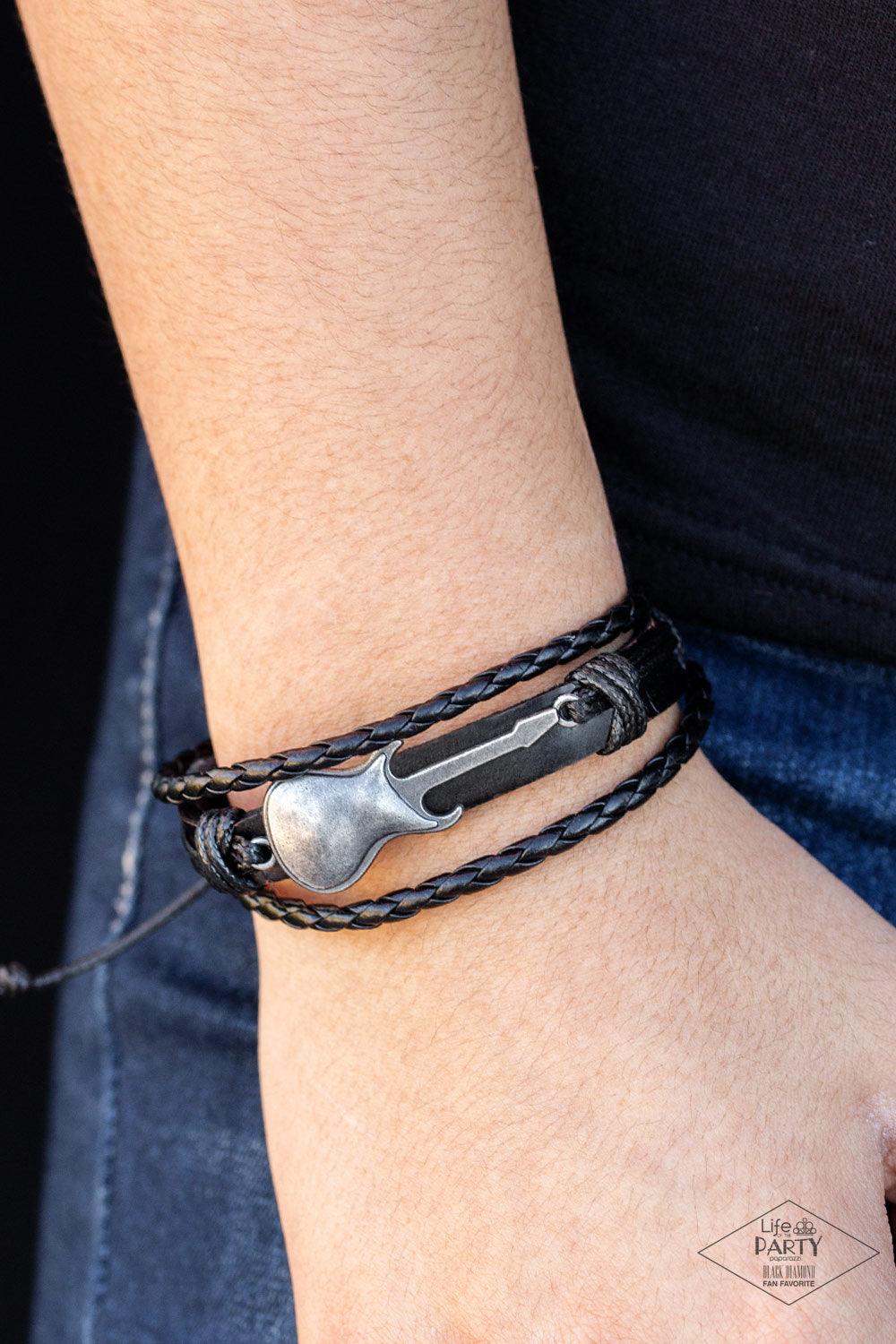 Paparazzi Accessories Lead Guitar - Black Two strands of braided leather cording join a rustic black leather band around the wrist. Shiny black cording wraps around a metallic guitar charm, knotting the centerpiece in place for an urban finish. Features a