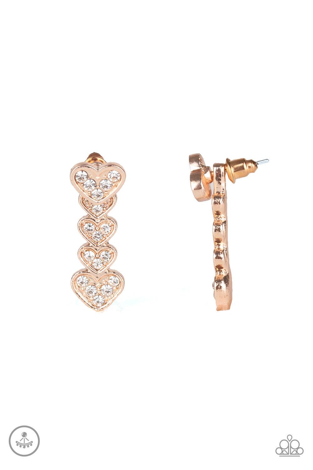 Paparazzi Accessories Heartthrob Twinkle - Rose Gold A white rhinestone encrusted rose gold heart attaches to a double-sided post, designed to fasten behind the ear. Stacked in gradually increasing white rhinestone encrusted heart frames, the glittery dou