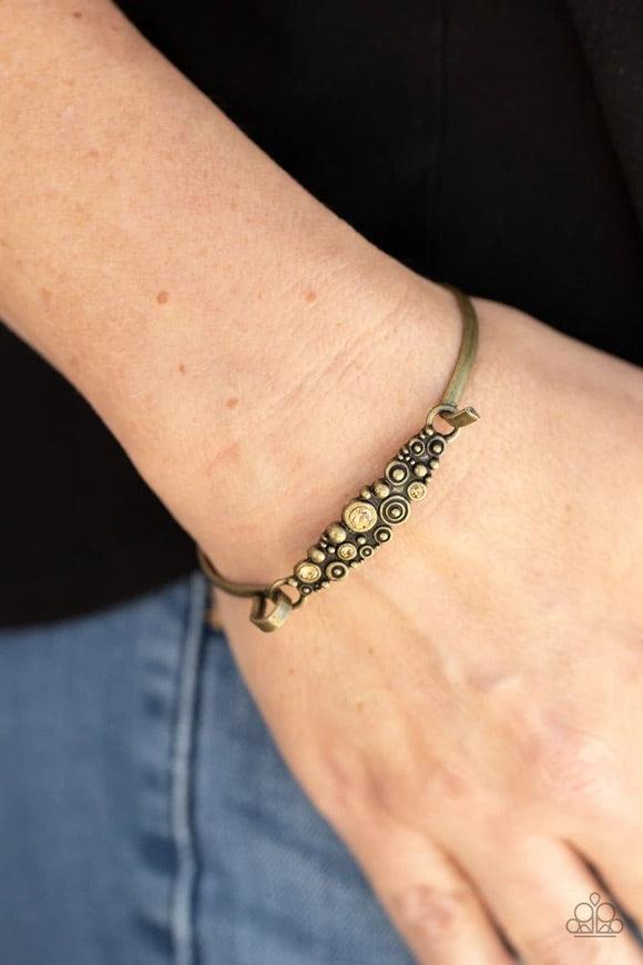 Paparazzi Accessories Bubbling Whimsy - Brass A cluster of engraved and antiqued brass swirls merge with topaz rhinestones and coalesce into a whimsical display across the wrist on a dainty brass cuff. Features a hook and eye closure. Sold as one individu