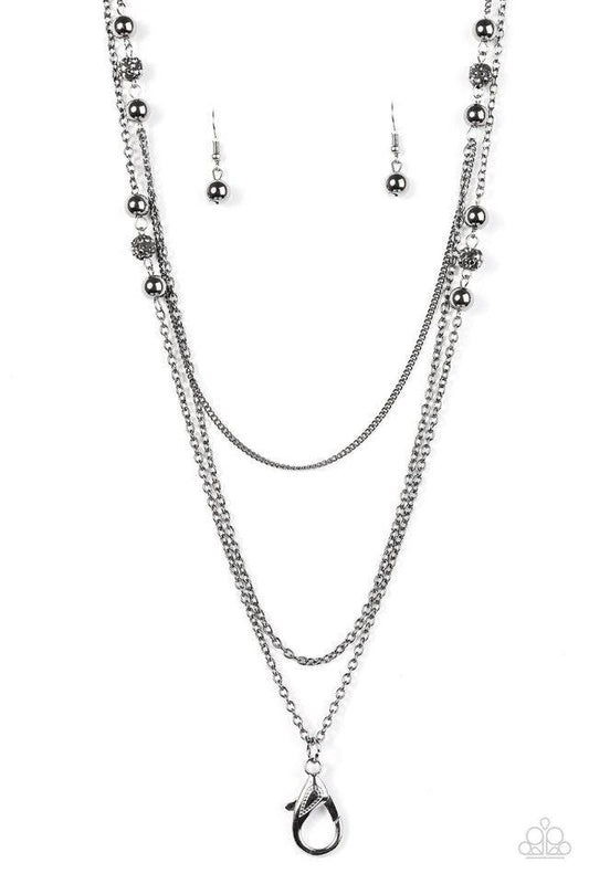Paparazzi Accessories Be In The Glow - Black *Lanyard Encrusted in glittery hematite rhinestones, sparkling black beads and shiny gunmetal beads trickle along three shiny gunmetal chains. A lobster clasp hangs from the bottom of the design to allow a name