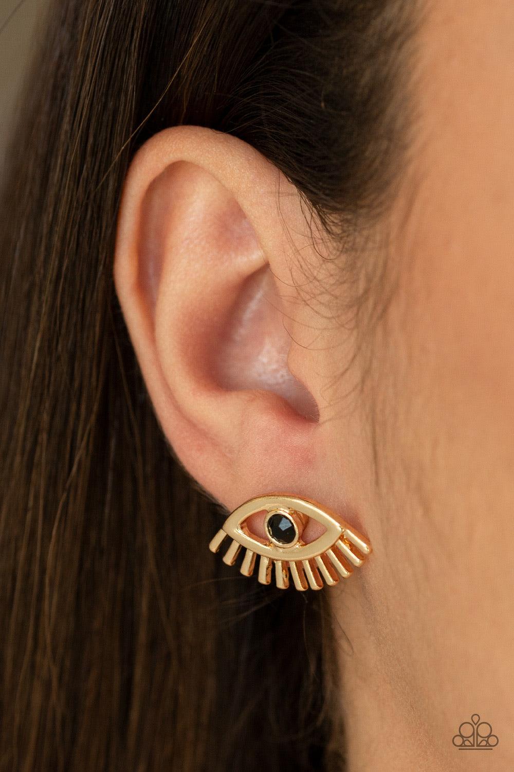 Paparazzi Accessories Don’t Blink - Gold A dainty black rhinestone is pressed into the center of a gold eye-shaped frame for a funky fashion. Earring attaches to a standard post fitting. Jewelry
