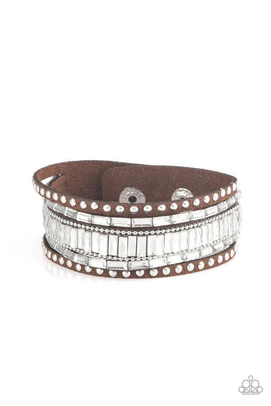 Paparazzi Accessories Rock Star Rocker - Brown Shiny silver studs, dainty silver ball chains, and edgy white emerald-cut rhinestones race along a spliced brown suede band for a rock star look. Features an adjustable snap closure. Sold as one individual br