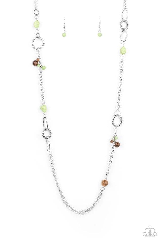 Paparazzi Accessories Sandstone Safari - Green A mismatched collection of brown wooden beads, green pebbles, hammered silver ovals, and dainty green stone beads haphazardly adorn sections of silver chain across the chest, creating an earthy seasonal flair