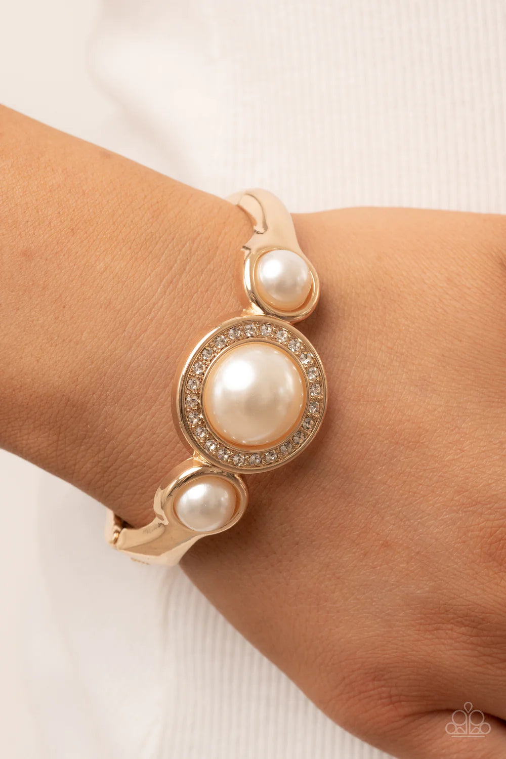 Paparazzi Accessories Debutante Daydream - Gold Encircled in a glitzy ring of glassy white rhinestones, an oversized white pearl is flanked by a pair of bubbly white pearl fittings atop a classic gold bangle-like bracelet for a timeless twist. Features a