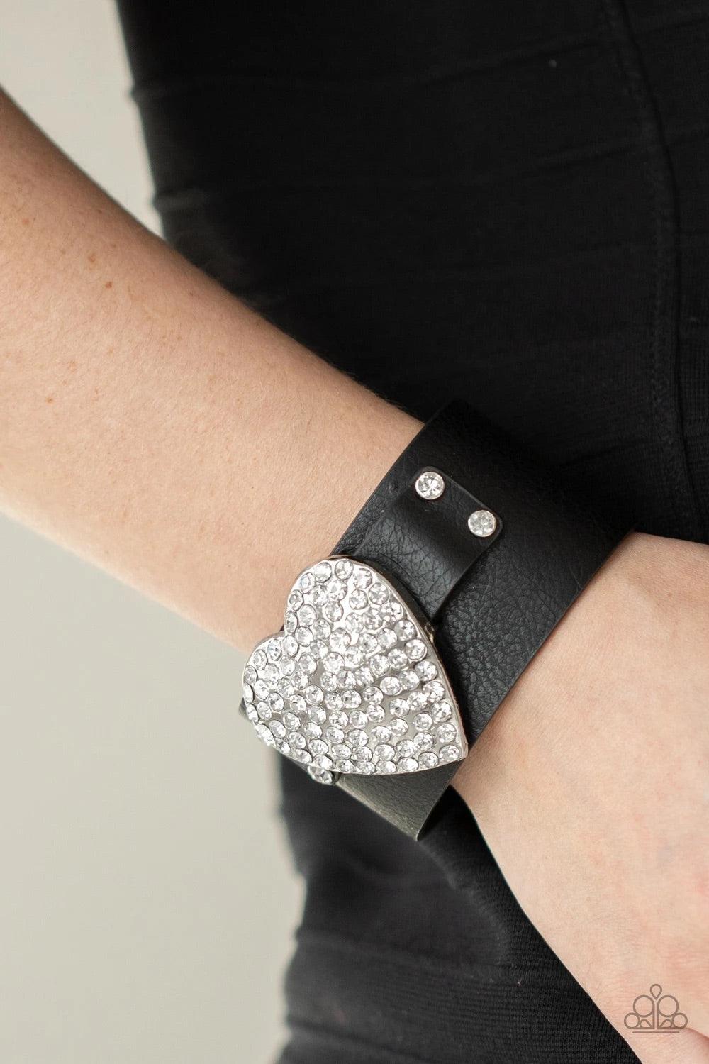 Paparazzi Accessories Flauntable Flirt - Black Encrusted in blinding white rhinestones, an oversized silver heart frame is studded in place across the front of a black leather band, creating a flirtatious centerpiece around the wrist. Features an adjustab