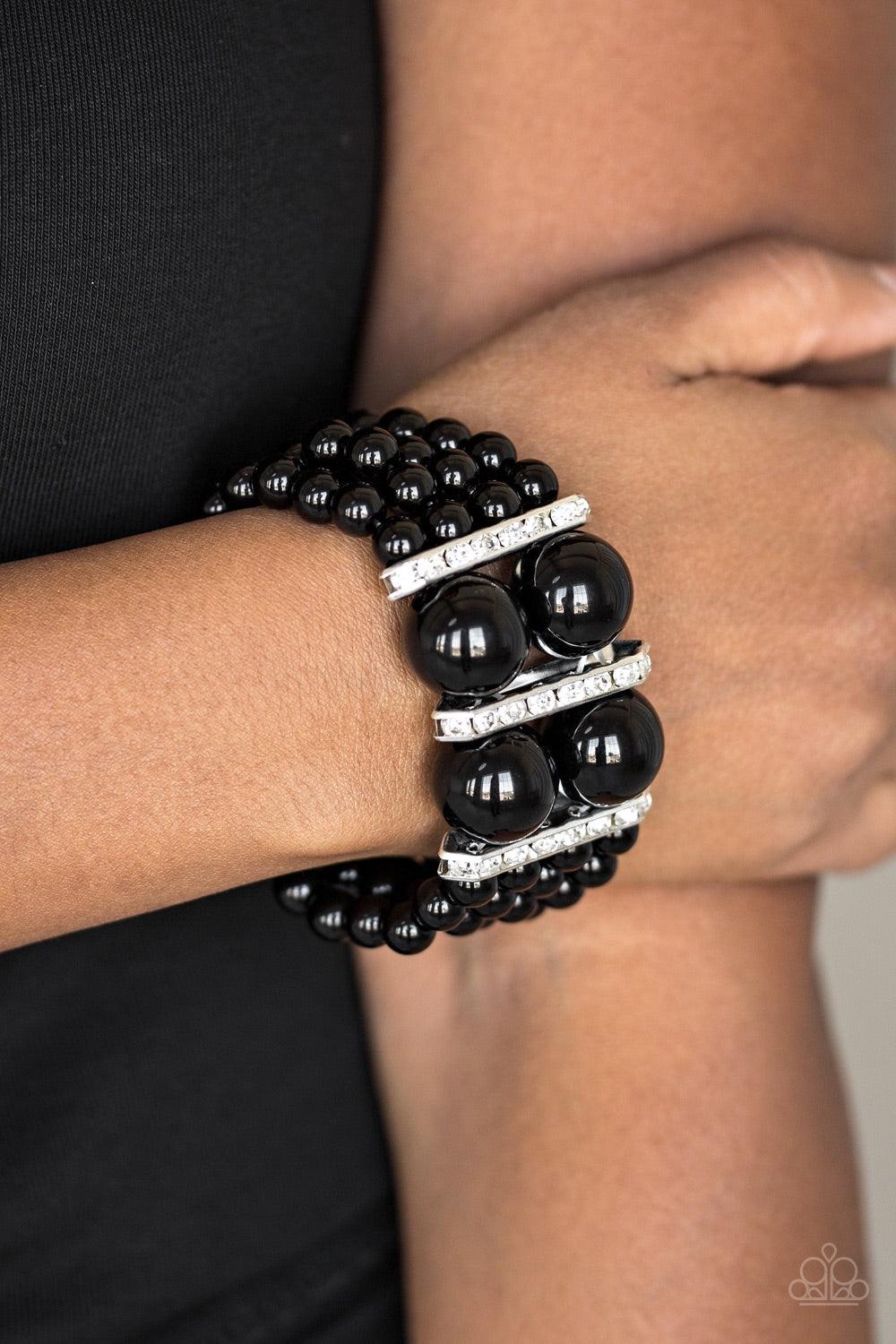 Paparazzi Accessories Romance Remix - Black Strands of shiny black beads are threaded along stretchy elastic bands and joined together by white rhinestone encrusted frames. The glittery frames combine with oversized beads at the center, adding a dramatic