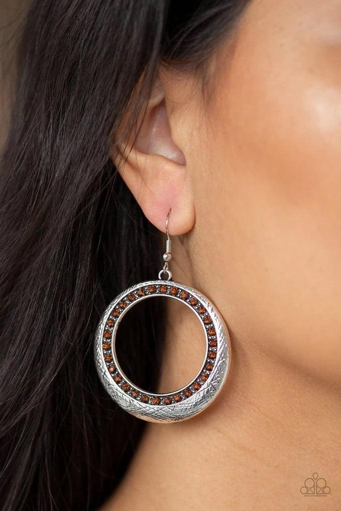 Paparazzi Accessories Go-Go Glow - Brown Delicately scratched in antiqued shimmer, a glistening silver hoop is encrusted in a ring of glittery topaz rhinestones for a refined look. Earring attaches to a standard fishhook fitting. Sold as one pair of earri