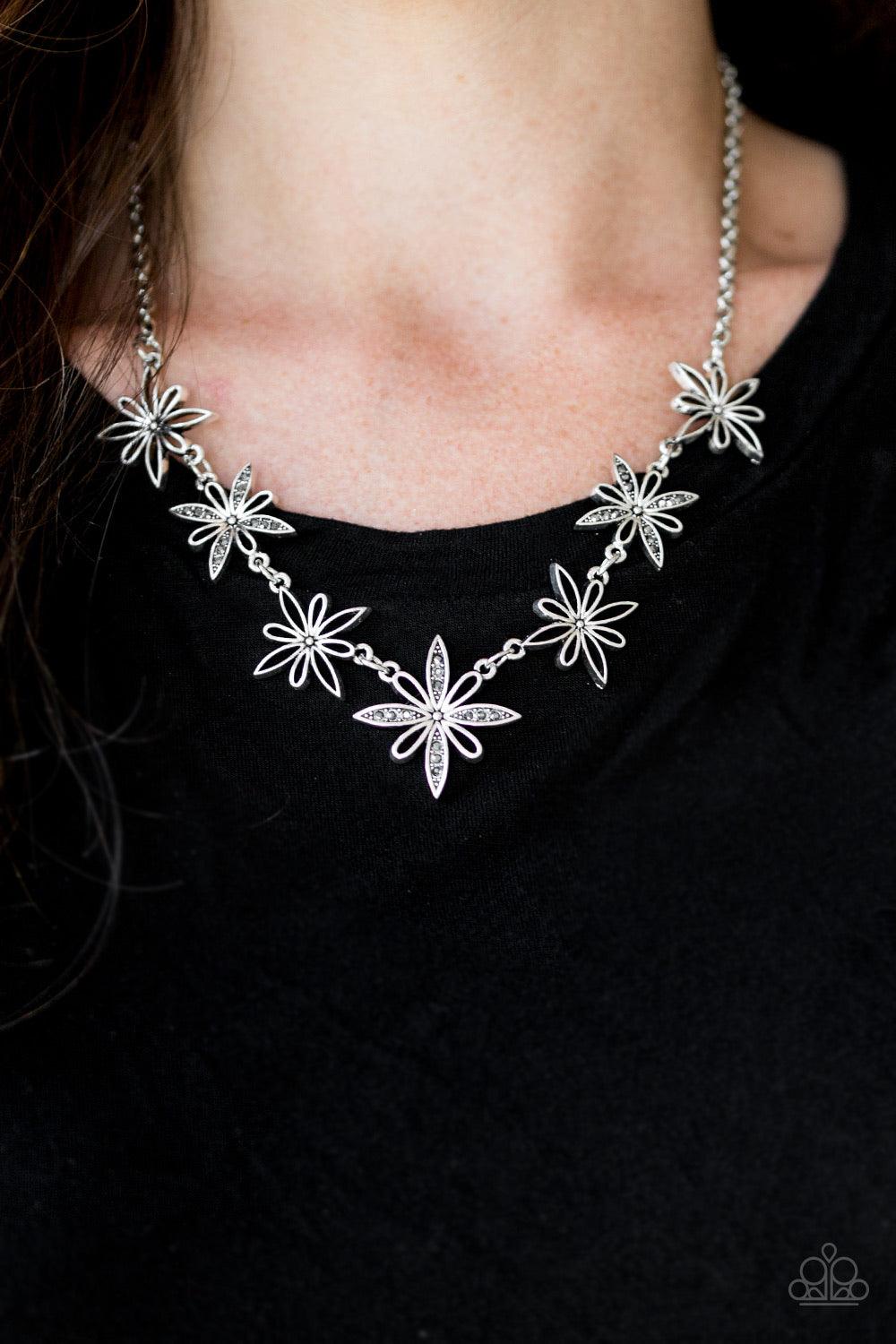 Paparazzi Accessories Decked Out In Daisies - Silver Airy silver floral charms link below the collar for a seasonal look. Dainty hematite rhinestones are encrusted along the petals of alternating floral frames for a glamourous finish. Features an adjustab