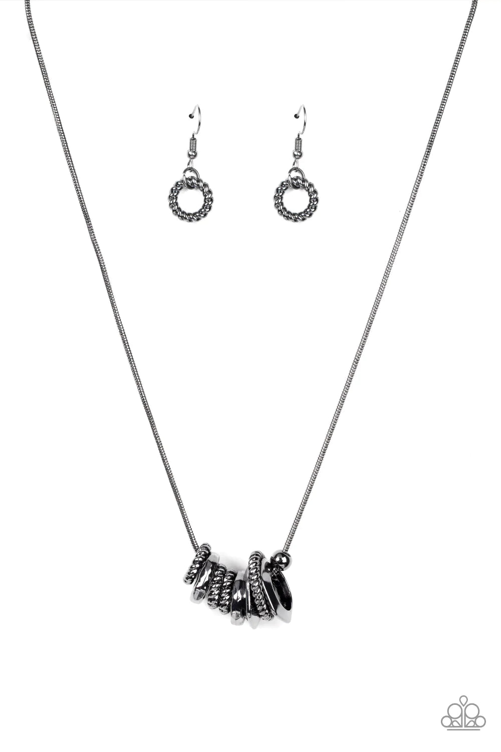 Paparazzi Accessories Mechanically Mischief - Black A gritty assortment of gunmetal ropelike rings, hammered gunmetal rings, and faceted gunmetal rings glide along a rounded gunmetal snake chain, creating an intense industrial collar below the collar. Fea