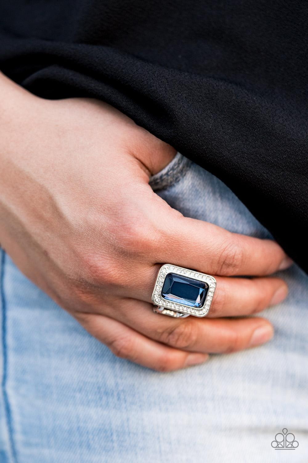 Paparazzi Accessories Crown Jewel Jubilee - Blue Featuring a regal emerald style cut, an oversized blue gem is bordered by a silver frame encrusted in glassy white rhinestones for a glamorous look. Features a stretchy band for a flexible fit Jewelry