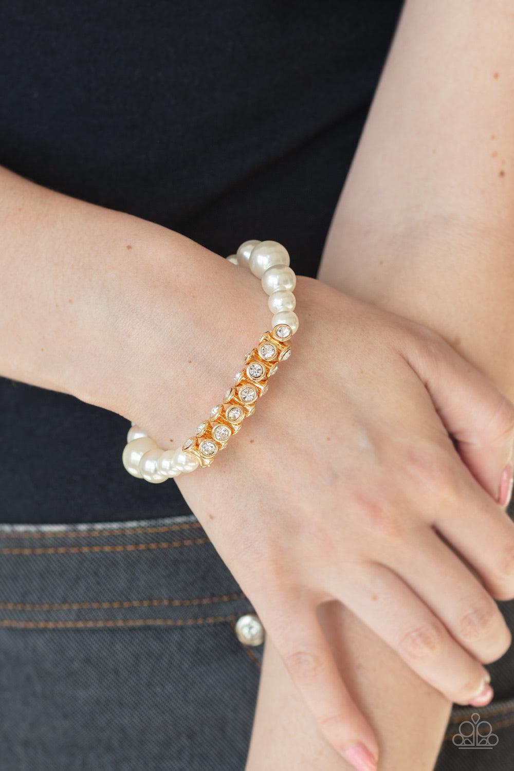 Paparazzi Accessories Traffic-Stopping Sparkle - Gold A collection of white pearls and white rhinestone dotted gold frames are threaded along stretchy bands around the wrist, creating a sparkling centerpiece. Jewelry
