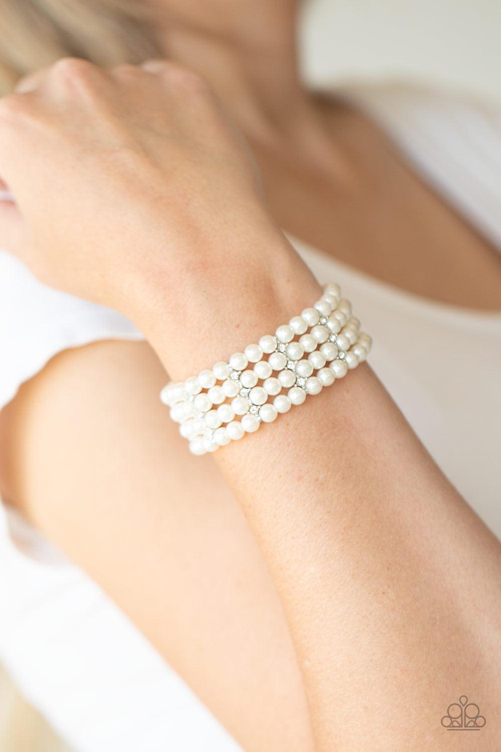 Paparazzi Accessories Stacked To The Top - White Held together by glittery white rhinestone encrusted silver fittings, row after row of white pearls are threaded along stretchy bands around the wrist for a timelessly stacked look. Sold as one individual b