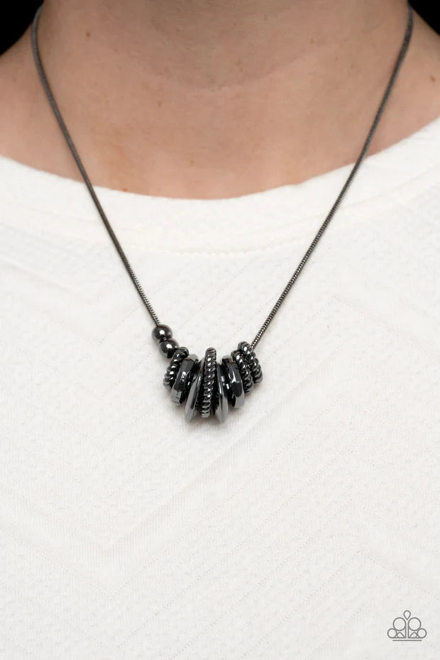 Paparazzi Accessories Mechanically Mischief - Black A gritty assortment of gunmetal ropelike rings, hammered gunmetal rings, and faceted gunmetal rings glide along a rounded gunmetal snake chain, creating an intense industrial collar below the collar. Fea