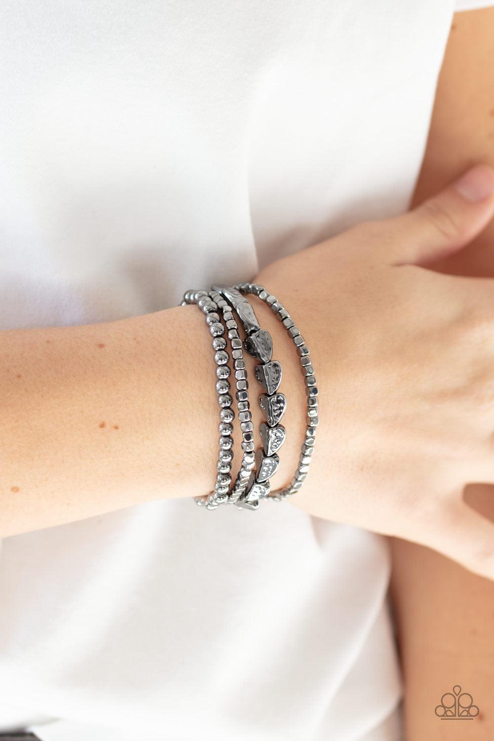Paparazzi Accessories Ancient Heirloom - Black A collection of gunmetal cubes, classic gunmetal beads, and hammered spade-like beading is threaded along stretchy bands around the wrist for a boldly stacked look. Jewelry