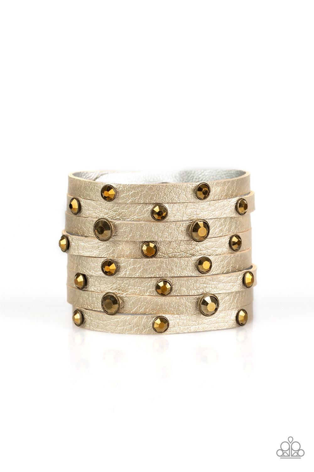 Paparazzi Accessories Go-Getter Glamorous - Brass Brushed in a metallic shimmer, a thick leather band has been spliced into eight strips across the wrist. Encased in sleek brass fittings, glittery aurum rhinestones are sprinkled across the center for a sa