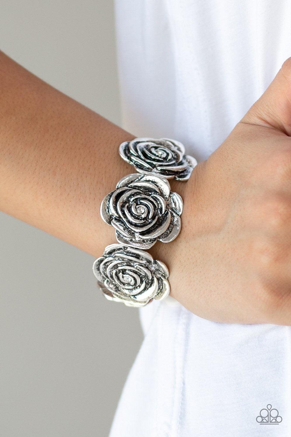Paparazzi Accessories Floral Flamboyancy - White Dotted with dainty white rhinestone centers, a collection of oversized silver rosebud frames are threaded along stretchy bands around the wrist for a whimsical look. Jewelry