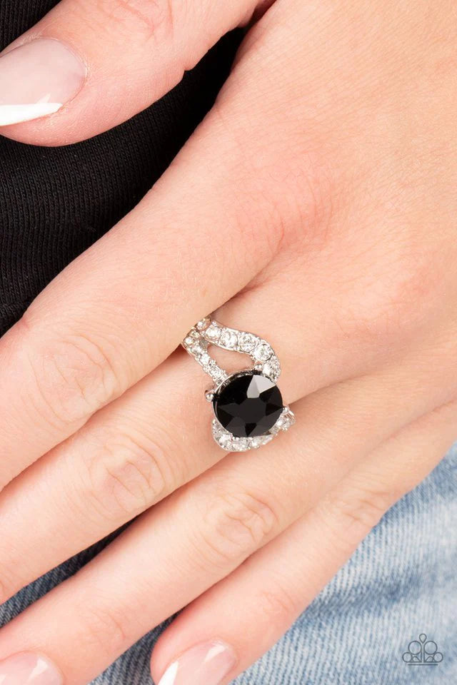 Paparazzi Accessories Blockbuster Boom - Black A faceted black rhinestone in a silver-prong setting makes a glamorously edgy centerpiece as it floats over the top of two silver bands. Encrusted with dainty white rhinestones, the wavy silver bands add dept