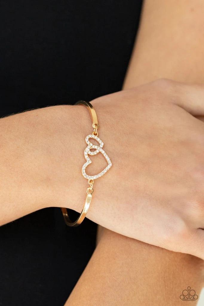 Paparazzi Accessories Cupid is Calling - Gold Encrusted in dainty white rhinestones, a charming pair of interlocking heart frames attach to two gold bars around the wrist, creating a flirty bangle-like bracelet. Features an adjustable clasp closure. Sold
