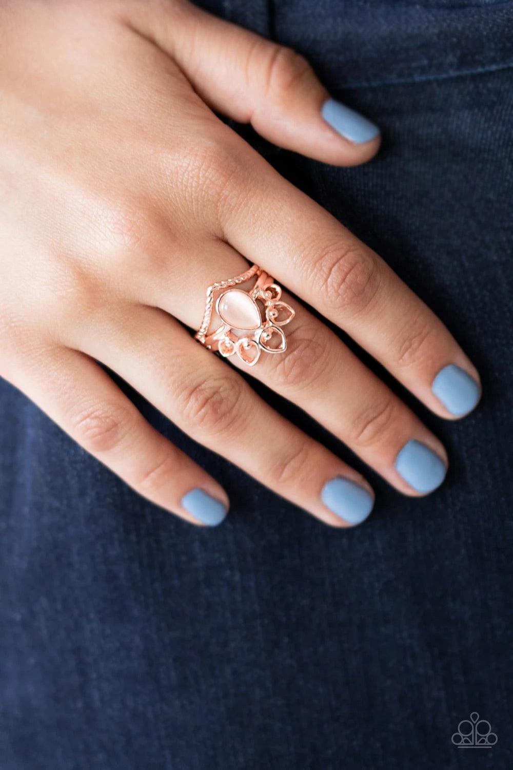 Paparazzi Accessories Serene Scene - Rose Gold Dotting the center of a dainty shiny gold band, a milky peach cat's eye stone teardrop is flanked between an angled rope-like band and an airy fan of studded rose gold petals. Features a dainty stretchy band