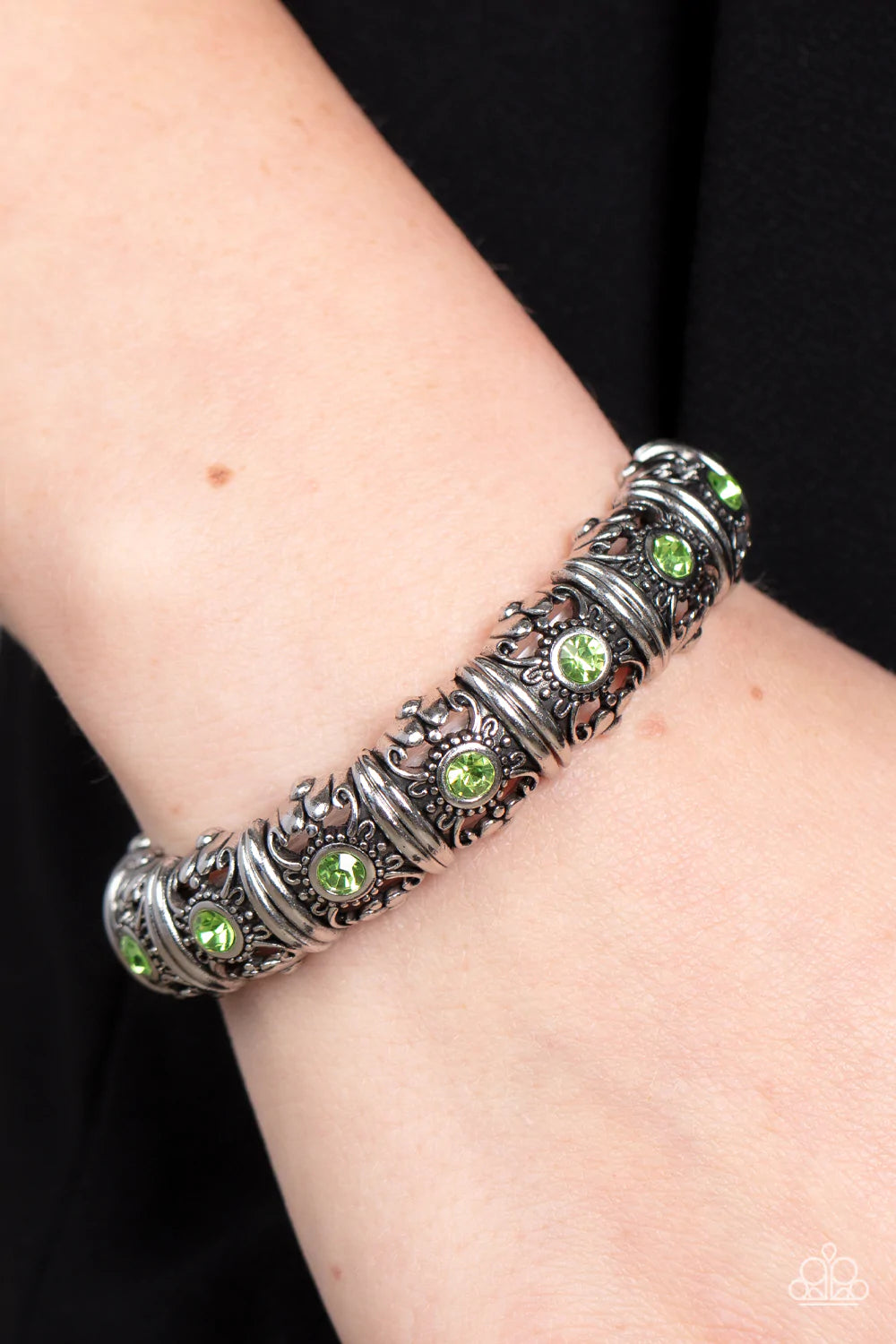 Paparazzi Accessories Angeless Glow - Green Centered around silver intricate, floral casings, green rhinestones glimmer on threaded stretchy bands around the wrist for an ageless look. Sold as one individual bracelet. Jewelry