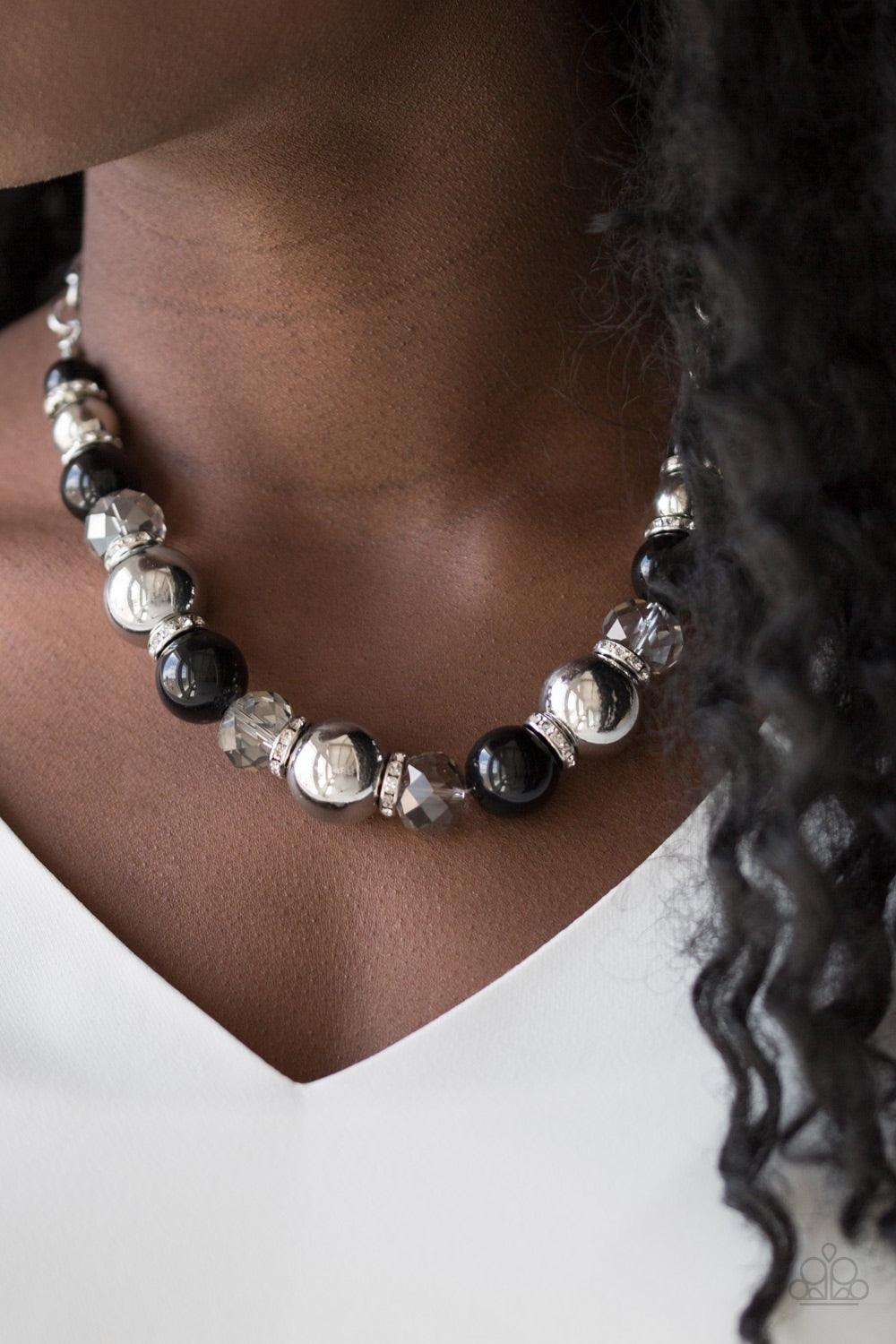 Paparazzi Accessories The Camera Never Lies - Black Oversized silver, smoky crystal-like, and polished black beads are threaded along an invisible wire below the collar for a glamorous look. White rhinestone encrusted rings are sprinkled between the drama