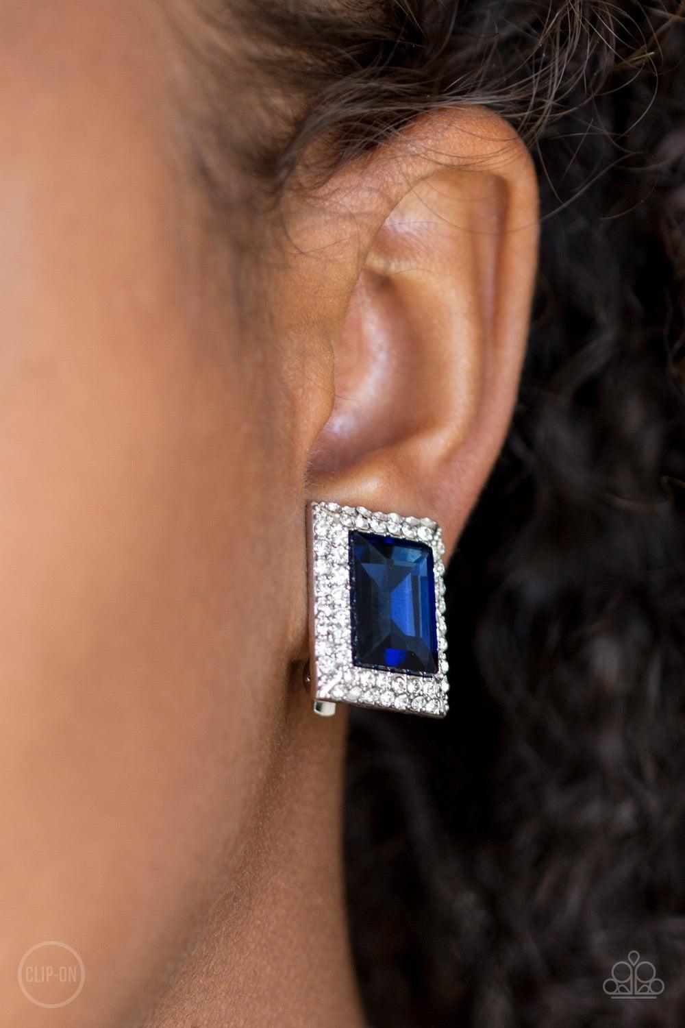 Paparazzi Accessories Crown Couture - Blue *Clip-On Featuring an elegant emerald style cut, a glittery blue gem is pressed into a rectangular frame radiating with sparkling white rhinestones for a regal fashion. Earring attaches to a standard clip-on fitt