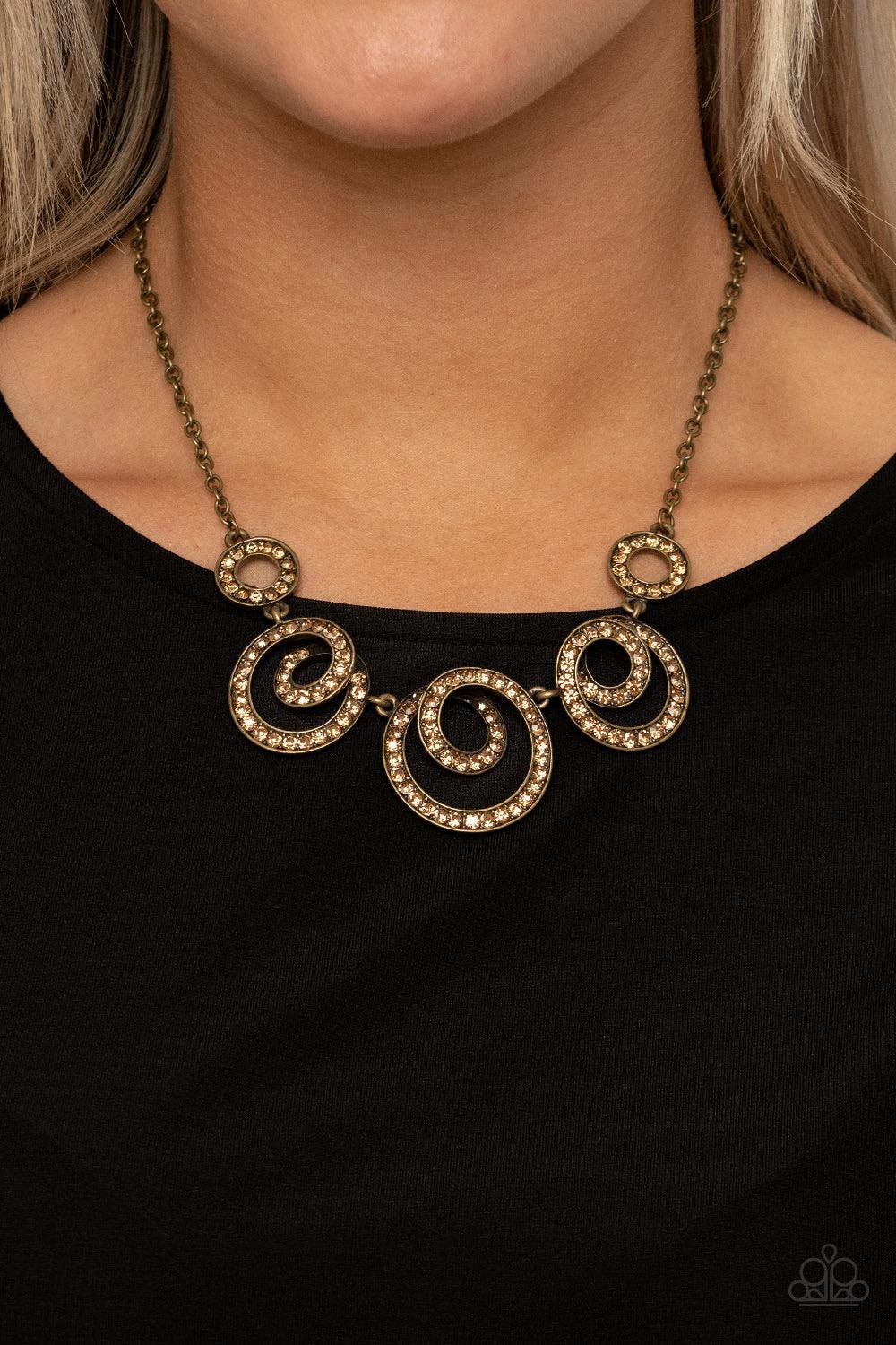 Paparazzi Accessories Total Head-Turner - Brass Encrusted in glassy topaz rhinestones, swirling brass frames delicately connect below the collar for a statement-making finish. Features an adjustable clasp closure. Sold as one individual necklace. Includes