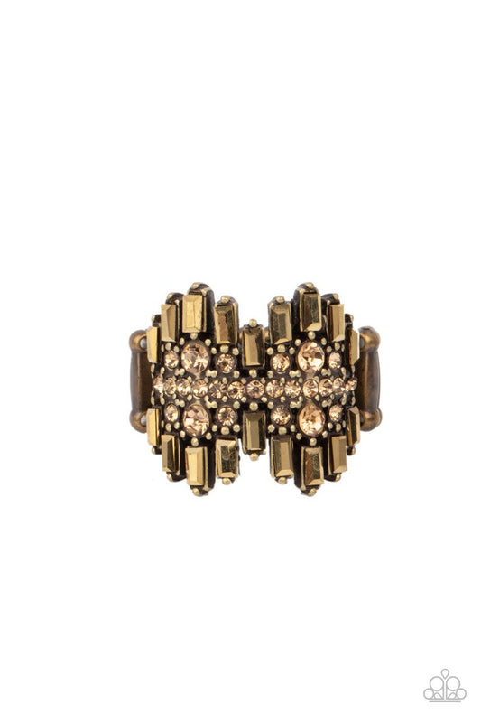 Paparazzi Accessories Urban Empire - Brass Staggered rows of emerald cut rhinestones flare out from the top and bottom of an explosion of aurum rhinestones, creating a smoldering statement piece atop the finger. Features a stretchy band for a flexible fit