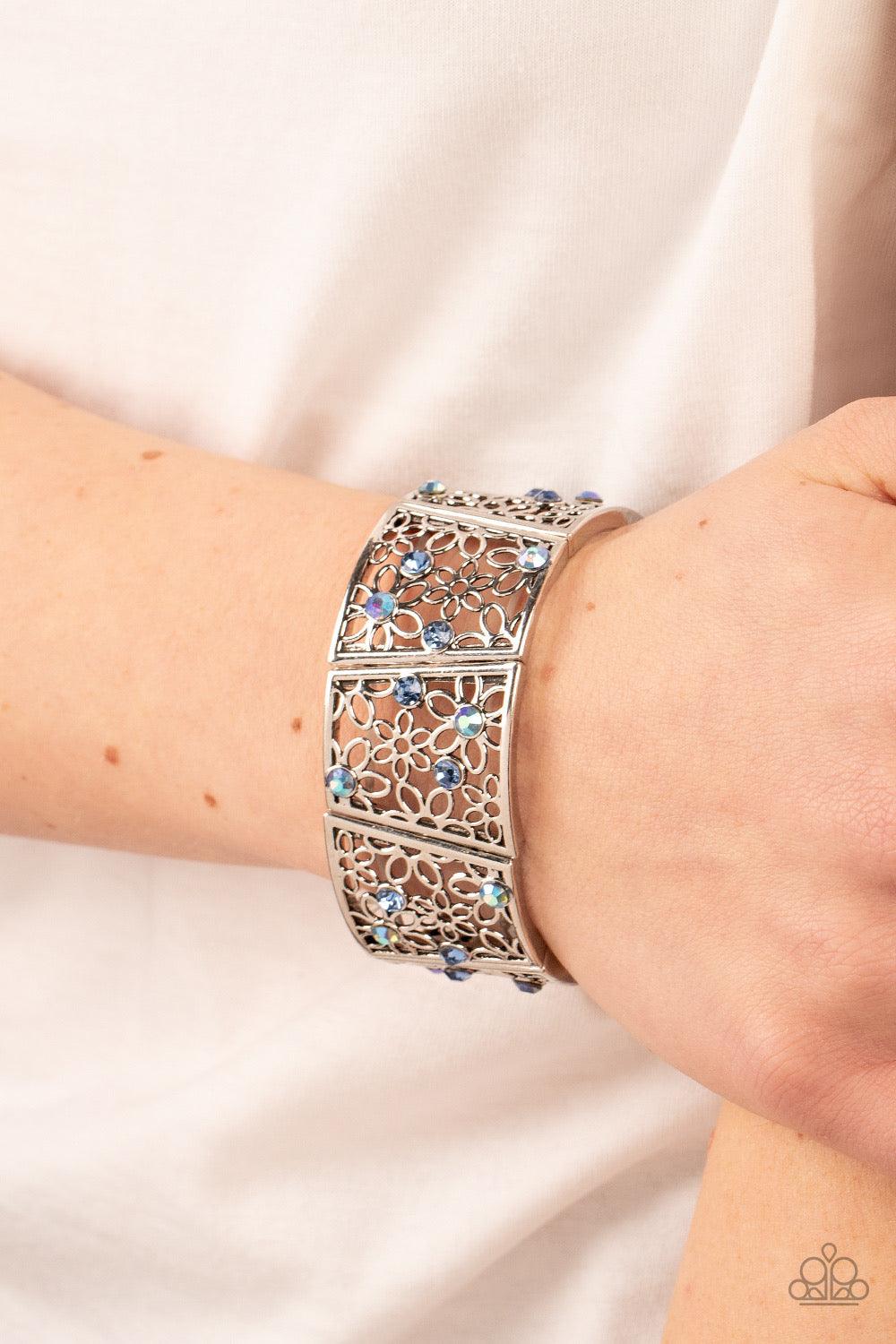 Paparazzi Accessories Spring Greetings - Blue Sporadically dotted with multicolored and iridescent rhinestones, an airy daisy pattern blooms inside trapezoidal silver frames that are threaded along stretchy bands around the wrist for a seasonal statement.
